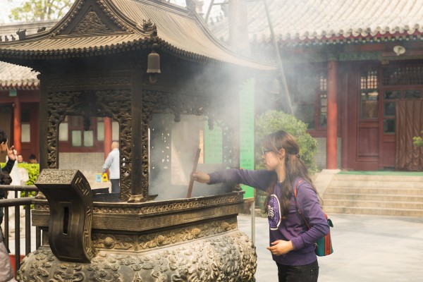 une jeune chinoise prie pour la bonne fortune au temple Guangji à Pékin, en Chine. (Crédit : Christoph Mohr / Picture alliance / Picture-Alliance / AFP).