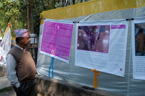 Le préfet du département de Banke, dans les jardins de la préfecture à Nepalgunj au Népal, devant une pancarte portant le témoignage d'une survivante du trafic d'êtres humains dans le cadre de l'exposition "Radiant Women".
