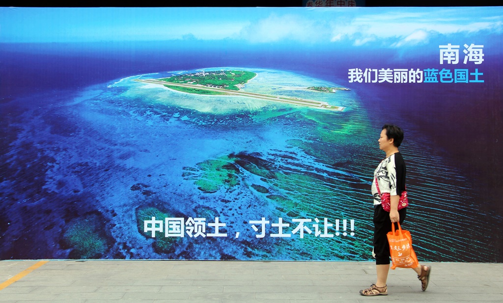 Un femme chinoise passe devant un poster géant de la mer de Chine du Sud avec le slogan "Ne cédons jamais un centimètre du territoire de la Chine !", dans un rue de Weifang dans la province du Shandong sur la côte nord-est de la Chine, le 14 juillet 2016.