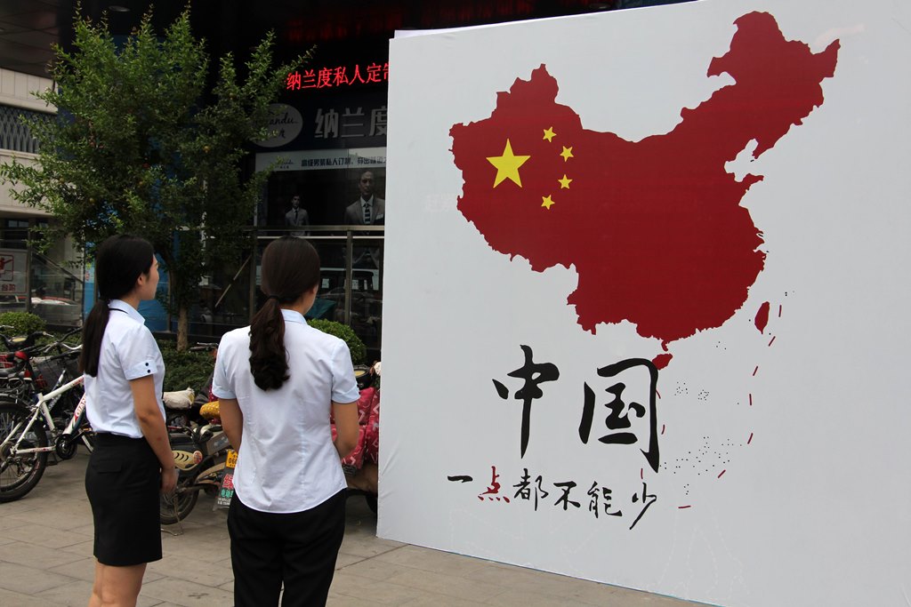 Des piétons regardent la carte de la Chine avec la "ligne à neuf traits" en mer de Chine du Sud et l'inscription en chinois "On ne peut rien enlever !", dans une rue de Weifang dans la province du Shandong sur la côte nord-est de la Chine, le 14 juillet 2016.