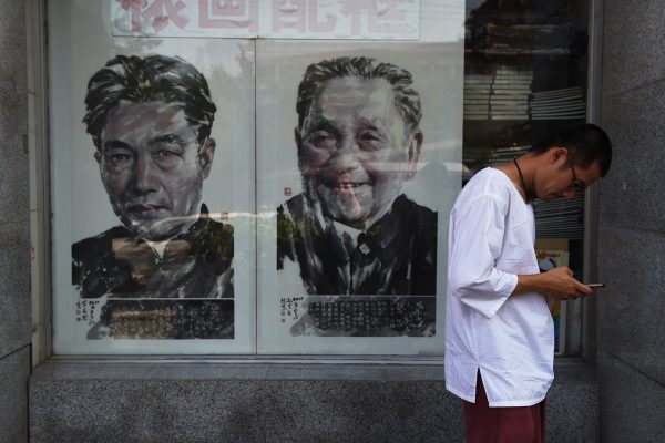 Un homme consulte son téléphone portable devant une affiche présentant les portrait de Deng Xiaoping (à droite) et de Xu Beihong (à gauche) à Pékin, le 10 août 2015.
