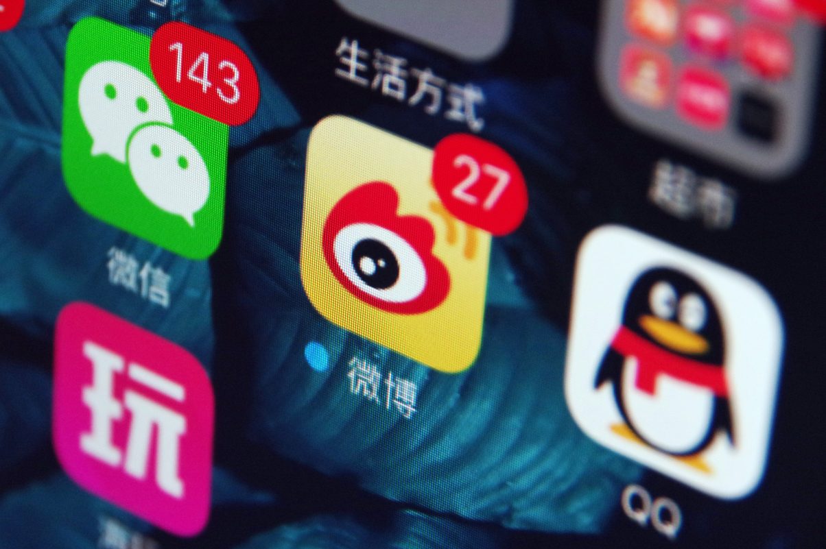 A gauche et à droite de l'écran d'un smartphone chinois, les icônes des applications de messagerie Wechat et QQ du groupe Tencent, et au centre, l'application de microblogs Weibo créée par Sina. (Crédits : Da qing / Imaginechina / via AFP)
