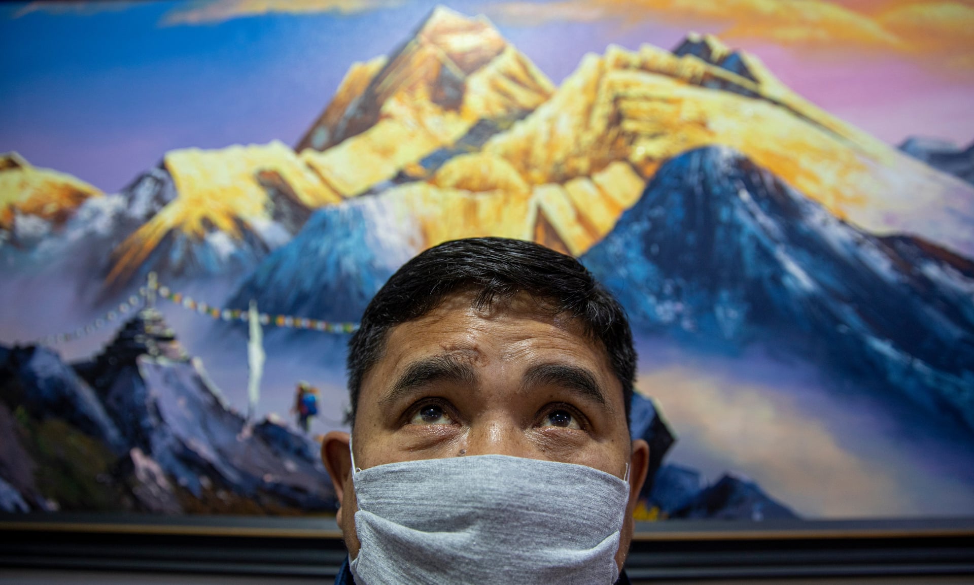 Le patron de la Freedom Art Gallery de Katmandou pose, masqué, face à un tableau du Mont Everest. Crédit : Narendra Shrestha/EPA, via The Guardian.