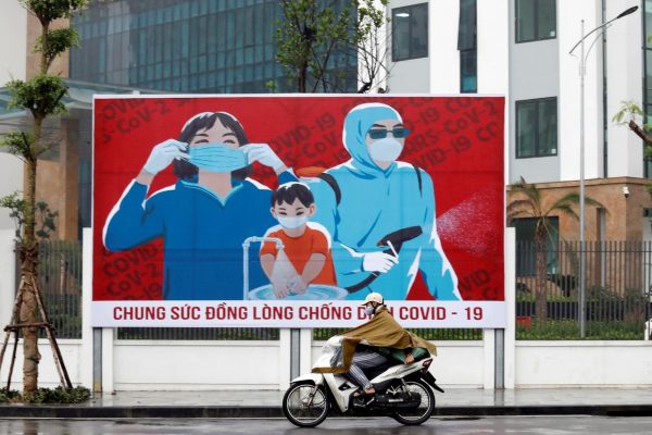 Un homme à scooter porte un masque tandis qu'il passe devant une affiche de propagande sur les mesures de précaution contre le coronavirus. Source : Reuters / Kham.